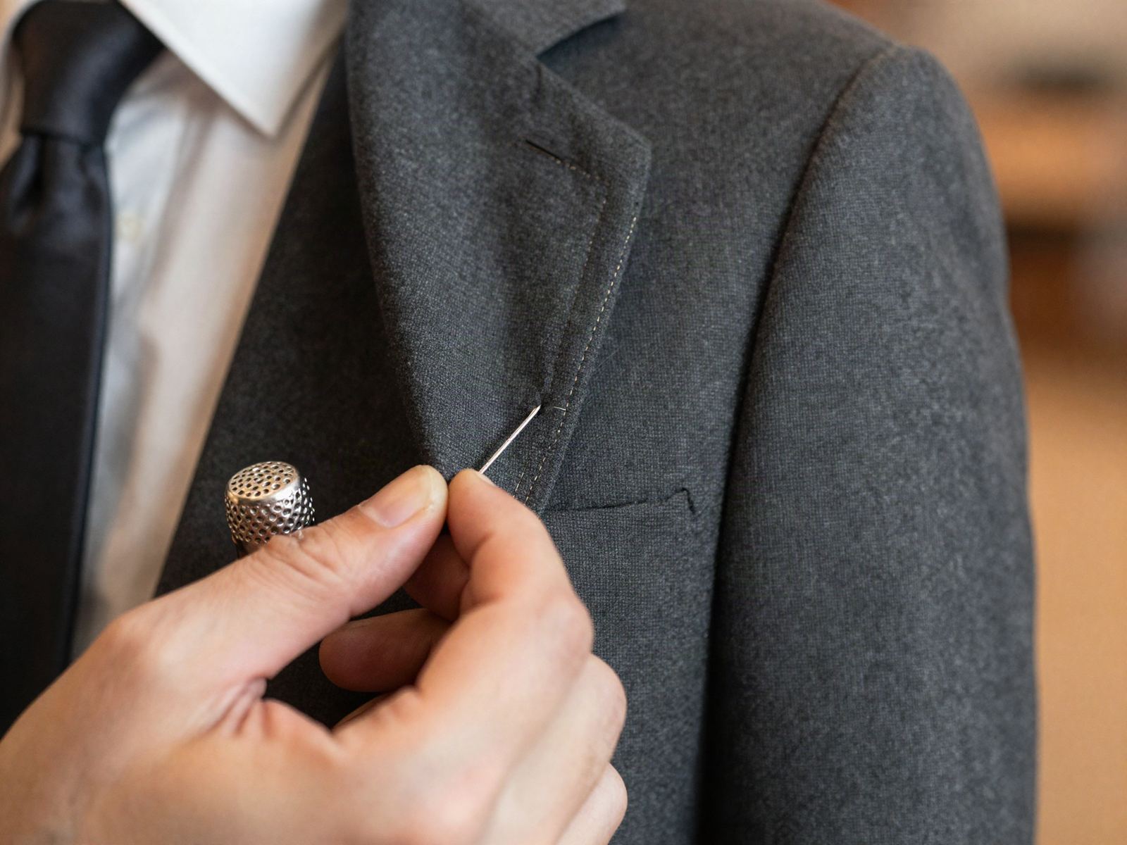 A tailor's hands hand-stitching the lapel of a jacket